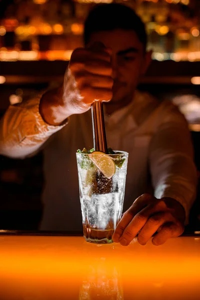 stock image Hand of male bartender masterfully press ingredients for mojito in transparent glass using muddler at bar. Close-up