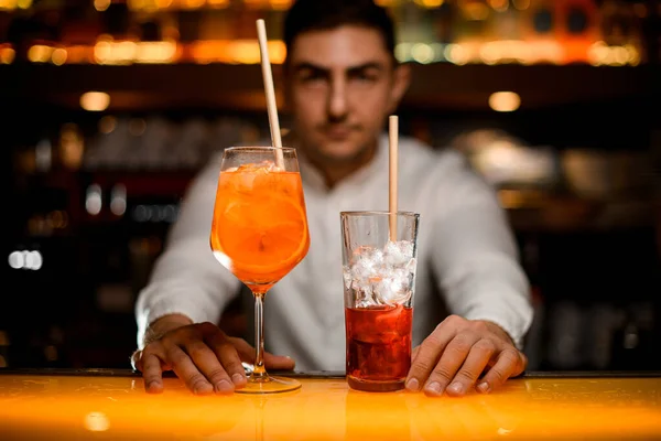 transparent glass with a cocktail with orange slices and a glass with an ice drink on the bar counter. Close-up. Male hands on bar