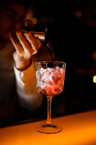 男性バーテンダーの手が鋼のジッガーからアルコール飲料を注ぐ氷と結晶ガラスに焦点を当て — ストック写真