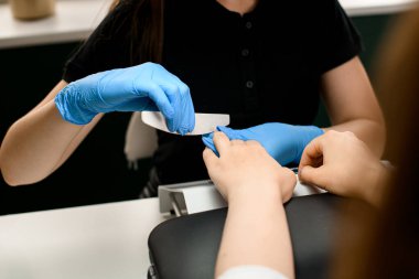 Yetenekli manikürcünün eldivenli ellerinin genç kadın tırnaklarını törpülediği harika bir yakın çekim görüntüsü.