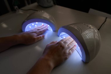 Kadın ellerine yakından bakınca, ultraviyole lambayla tırnaklarını kurutuyor. UV lambası jöle cilası manikür süreci. Salon prosedürü.