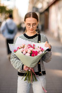 Güzel bir kadın elinde bir buket parlak pembe gül tutuyor ve ona bakıyor.