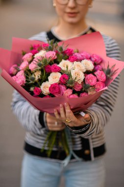 Beyaz, pembe güller ve kadının ellerinde devedikeni olan buket çiçeklerine yakından bakın.