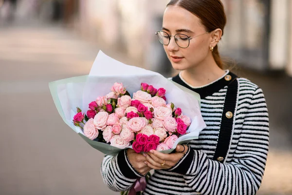 stock image beautiful woman holds bouquet of bright pink roses in wrapping paper in her hands and look at it