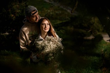 Yeşil çam dallarının arasından harika bir manzara. Aşık güzel bir çift, şefkatli bir erkek, bir kadına sarılıyor.