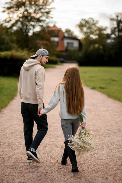 手に白い花の長い髪と花束を持つ女性の愛の若いカップルの後ろのビューと男は通りを歩いて お互いを見て ラブストーリー — ストック写真