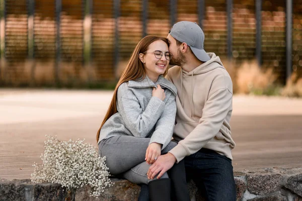 陽気な若い女性と男が屋外に座っている 彼女にキスして ラブストーリー 愛の幸せなカップル ロマンチックなデート — ストック写真