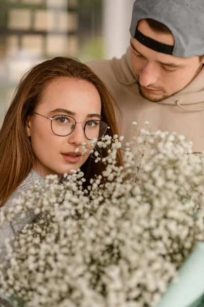 花束と男が彼女を見ているメガネのハンサムな女性の肖像画 接近中だ ロマンチックなデートだ ラブストーリー — ストック写真