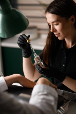 Kozmetik şişeli, pipetli ve elinde siyah eldivenli sıvı olan kadın güzellik uzmanı. Çivi bakımı konsepti. Güzellik salonu.
