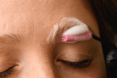 Kadının yüzünün bir kısmı, temizleme köpüğünün özel bir fırçayla dikkatlice uygulandığı kaşlara yakın plan.