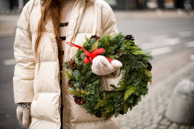 Güzel, yuvarlak bir çelenk olan eşkıya ve ladin, ceket ve eldiven giymiş bir kadının ellerinde.