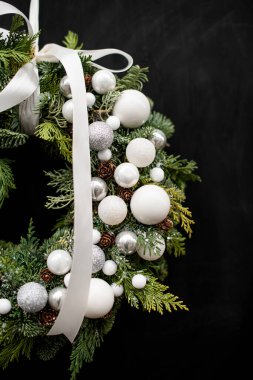 Beyaz toplar ve koyu arkaplanda kurdeleyle süslenmiş ladin ve thuja dallarından oluşan güzel doğal Noel çelenklerinin kesilmiş fotoğrafı.