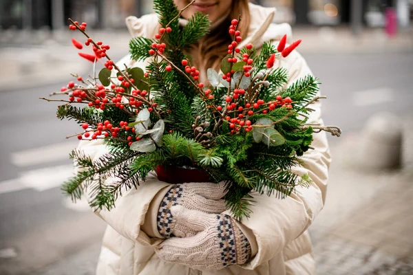 手に赤い果実とユーカリの葉を持つスプルースの枝や小枝のポットで美しいクリスマスの花の配置のクローズアップビュー — ストック写真