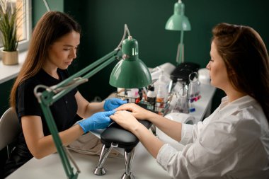 Odaklanmış kadın manikürcü kadın müşterinin ellerine ve tırnaklarına bakıyor. Profesyonel güzellik salonunda..