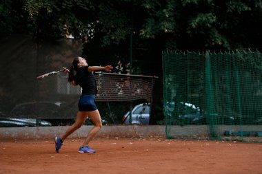 Sırtında tenis raketi olan aktif bayan tenisçinin yan görüntüsü. Açık hava tenis antrenmanı..