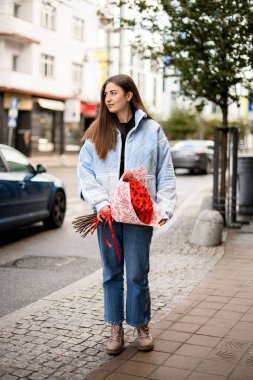 Elinde bir buket kırmızı gülle güzel esmer kadın sokakta duruyor.