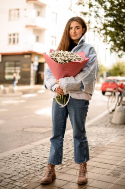 Elinde bir buket beyaz kasımpatı ya da papatya çiçeğiyle güzel esmer kadının tam boy portresi.