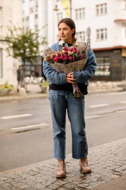 Yakışıklı esmer kadın portresi, elinde çiçek buketi, elinde ambalaj kağıdıyla caddede.