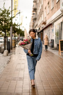 Elinde ambalaj kağıdıyla caddede yürüyen güzel çiçekli esmer kadın manzarası