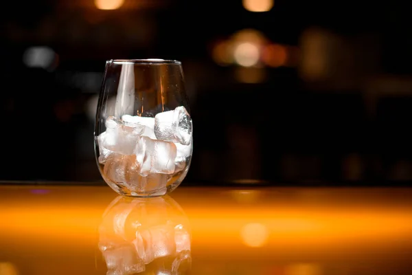 close-up of transparent glass with ice cubes on the bar counter on blurred background. Copy space
