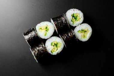 Top view on classic vegetarian kappa maki sushi rolls with fresh cucumbers and rice wrapped in nori on dark background