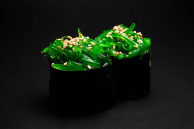 Close-up of japanese gunkan sushi with chukka and sesame seeds wrapped in nori seaweed. Side view of rolls gunkan chuka maki on dark background.