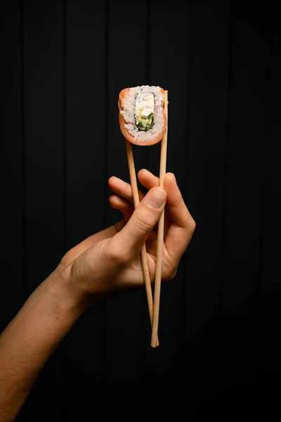 Tasty Philadelphia Roll Hand Holding Bamboo Chopsticks Dark Background One — Stok fotoğraf