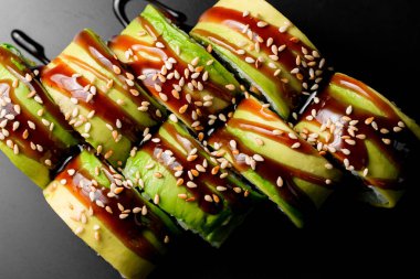 Close-up top view of green dragon sushi rolls with salmon, avocado, cucumber and green caviar. Traditional asian rice sushi healthy seafood. Dark background