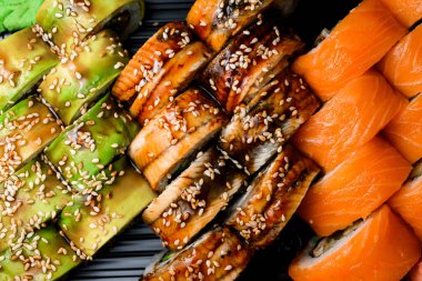 Close-up top view on set of Philadelphia sushi rolls with soya sauce and sesame and rolls with salmon and Green dragon sushi rolls. Cropped photo