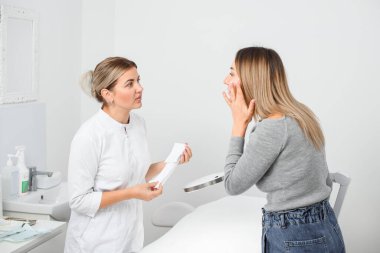 professional female cosmetologist performs facial examination procedure at cosmetology clinic. Beautiful caucasian woman in beauty salon