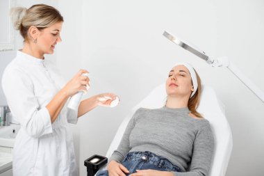 Beautician clean female face before procedure, patient lying on couch in beauty clinic. Cosmetology concept.