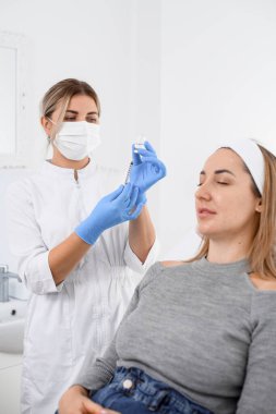 view on female patient on couch in beauty clinic and female cosmetologist in blue latex gloves on background. Cosmetology concept.