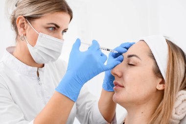 attractive caucasian woman getting botox cosmetic injection in a forehead from professional female cosmetologist. Concept of cosmetology, beauty.