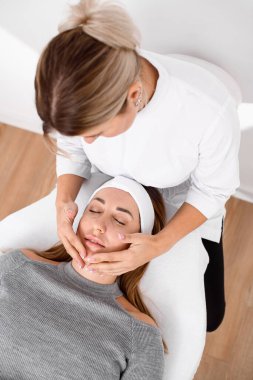 high angle view of professional cosmetologist doing face massage to woman at beauty salon. Concept of cosmetology, beauty.