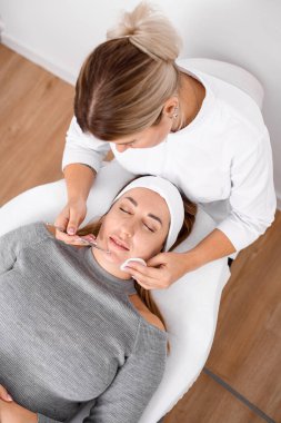 top view of cosmetologist in medical gloves removing blackheads at female face using tools and cotton pad