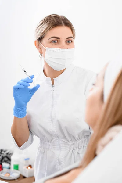 professional woman doctor in protective medical mask with blue latex gloves on her hands holds a syringe with liquid. Concept of cosmetology, beauty.