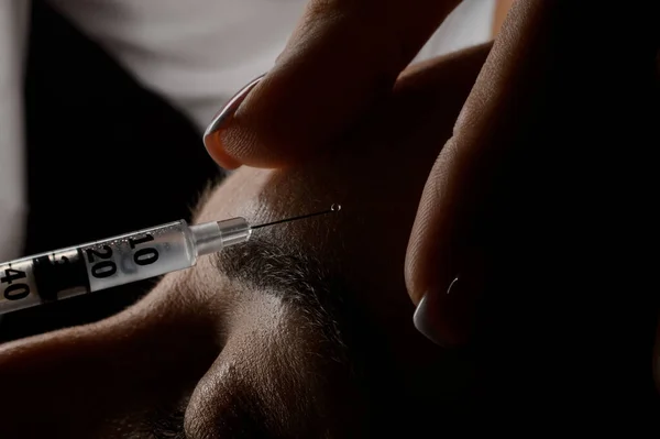 Close-up view of caucasian female forehead and a syringe with a needle making an injection of botox in the skin.