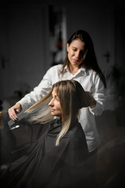 Professional hairdresser is combing the hair of beautiful young female client in modern beauty and hair salon.