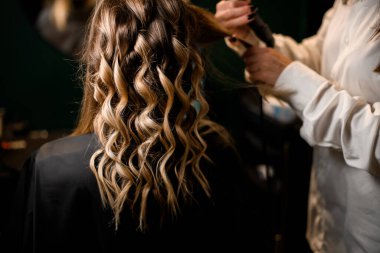 selective focus on beautiful curled strands of female hair. Stylist curls hair with modern clipless curling iron. Cropped photo. Hairstyle