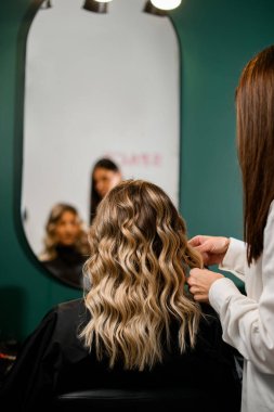 back view of woman with perfect hairstyle of curl hair and female hairdresser in hair salon