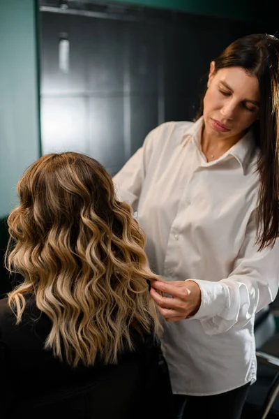 rear view of woman with perfect hairstyle of curl hair and female hairdresser in hair salon