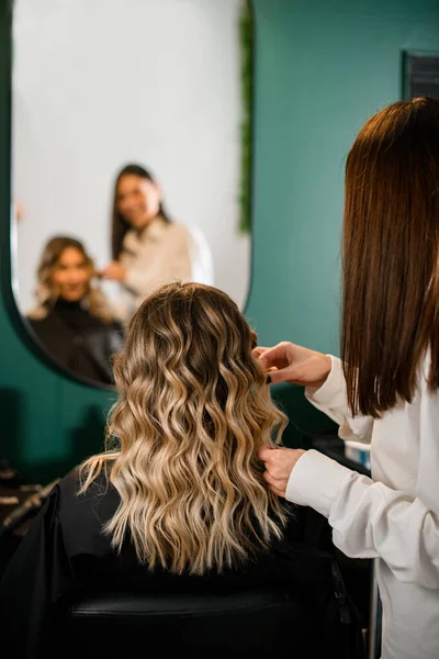 great rear view of woman with perfect hairstyle of curl hair and female hairdresser in hair salon