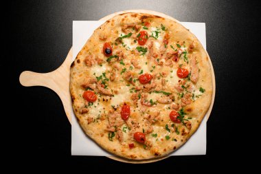 top view on tasty hot pizza with cherry tomatoes and chicken garnished by fresh green on a black table
