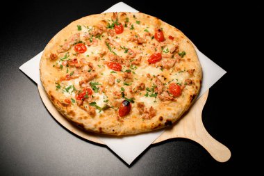 view on delicious hot pizza with cherry tomatoes and chicken garnished by fresh green on a black table