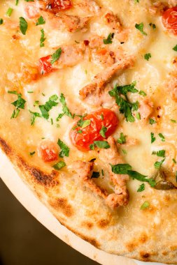 Close-up part of delicious hot pizza with cherry tomatoes and chicken garnished by green. Traditional italian dish