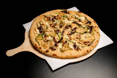 view of tasty hot vegetarian vegetable pizza with mushrooms walnuts and zucchini slices on black table.