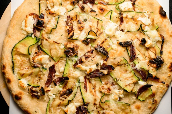 photography of tasty vegetarian vegetable pizza with mushrooms walnuts and zucchini slices. Close-up top view