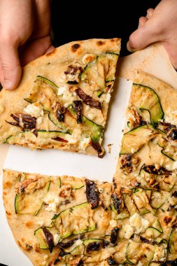 great top view on delicious pizza with topping of mushrooms walnuts and zucchini slices and hand taking a piece of it. Traditional italian cuisine