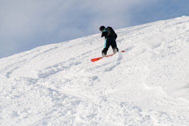 sportive man on snowboard riding freeride on white powder snow down the slope against the backdrop of the sky