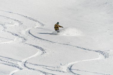 great view of a snow-covered mountain slope with traces of a snowboard and a man on a snowboard slides down